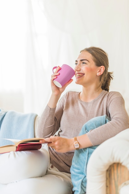 Foto gratuita sonriente joven bebiendo café mientras está sentado en el sofá