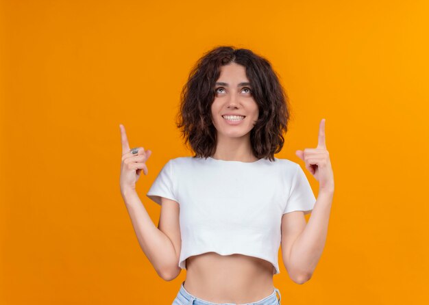 Foto gratuita sonriente joven bella mujer apuntando con los dedos hacia arriba en la pared naranja aislada con espacio de copia