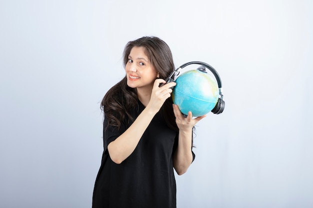 Sonriente a joven y bella mujer de pie y sosteniendo un globo en auriculares.