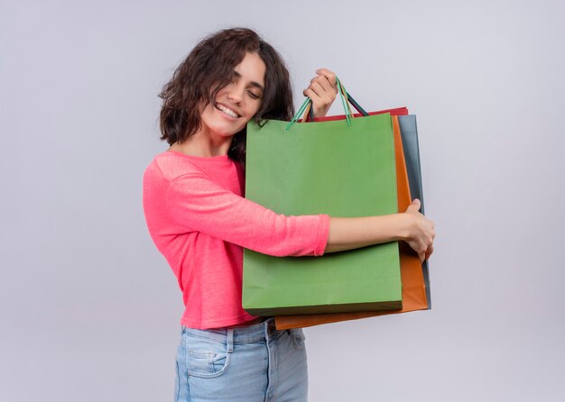 Sonriente joven bella mujer sosteniendo bolsas de papel en la pared blanca aislada