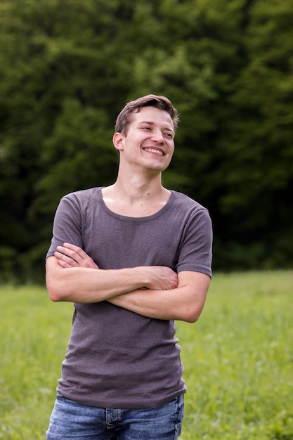 Sonriente joven con los brazos cruzados en la naturaleza