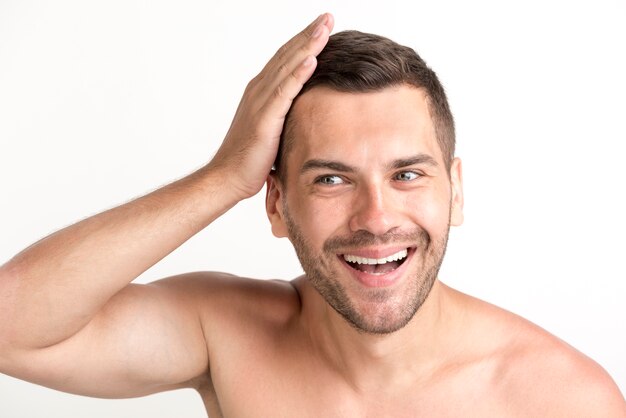 Sonriente joven sin camisa tocando su cabello sobre fondo blanco