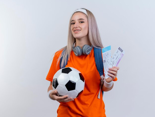 Sonriente joven caucásica deportiva con auriculares alrededor del cuello con diadema de mochila