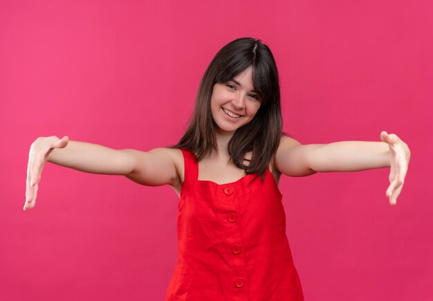 Sonriente joven caucásica finge sostener algo sobre fondo rosa aislado