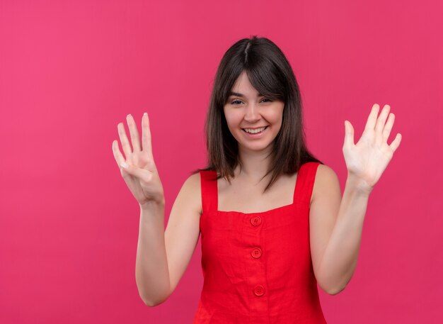 Sonriente joven caucásica mostrando nueve con los dedos y mirando a cameraon fondo rosa aislado