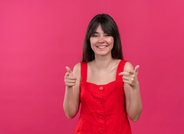 Sonriente joven caucásica señalando con el dedo a la cámara y mirando a la cámara sobre fondo rosa aislado con espacio de copia