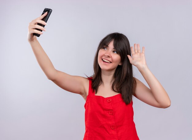 Sonriente joven caucásica sosteniendo el teléfono y mostrando la mano vacía mirando el teléfono sobre fondo blanco aislado