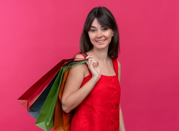 Sonriente joven caucásica sostiene paquetes tirándolos al hombro sobre fondo rosa aislado