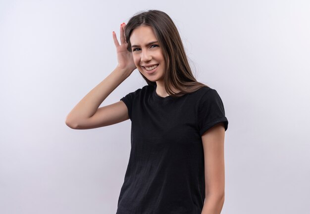 Sonriente joven caucásica vestida con camiseta negra mostrando escuchar gesto sobre fondo blanco aislado