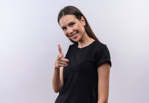Sonriente joven caucásica vestida con camiseta negra que le muestra gesto sobre fondo blanco aislado