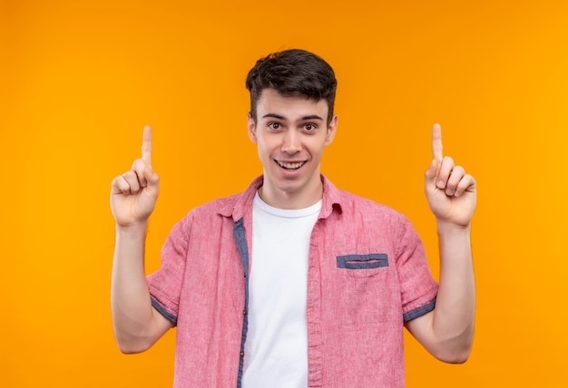 Sonriente joven caucásico con camisa rosa apunta hacia arriba sobre fondo naranja aislado