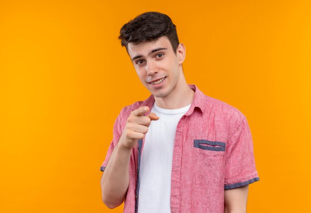 Sonriente joven caucásico con camisa rosa que le muestra gesto sobre fondo naranja aislado
