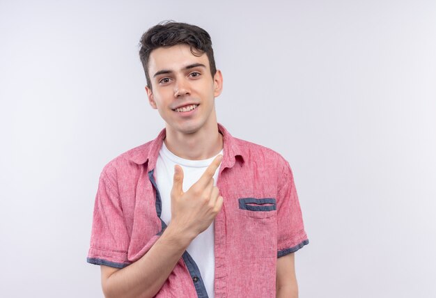 Sonriente joven caucásico vistiendo camisa rosa apunta al lado sobre fondo blanco aislado