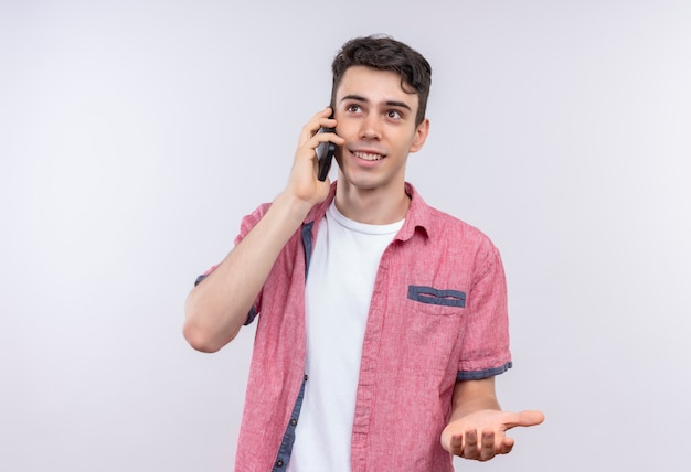 Sonriente joven caucásico vistiendo camisa rosa habla por teléfono sobre fondo blanco aislado