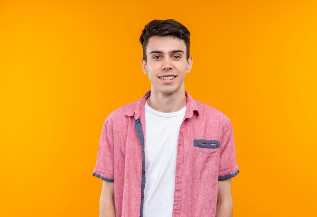 Sonriente joven caucásico vistiendo camisa rosa sobre fondo naranja aislado