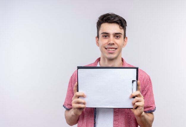 Sonriente joven caucásico vistiendo camisa rosa sosteniendo el portapapeles sobre fondo blanco aislado