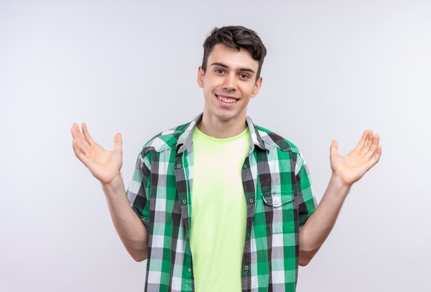 Sonriente joven caucásico vistiendo camisa verde extiende las manos sobre fondo blanco aislado