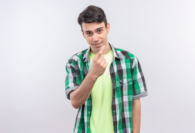 Sonriente joven caucásico vistiendo camisa verde mostrando ven aquí gesto sobre fondo blanco aislado