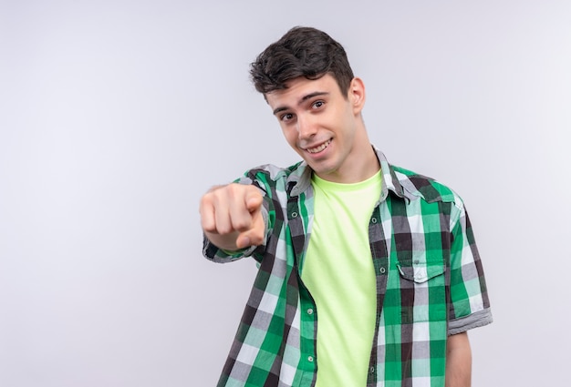 Sonriente joven caucásico vistiendo camisa verde que le muestra gesto sobre fondo blanco aislado