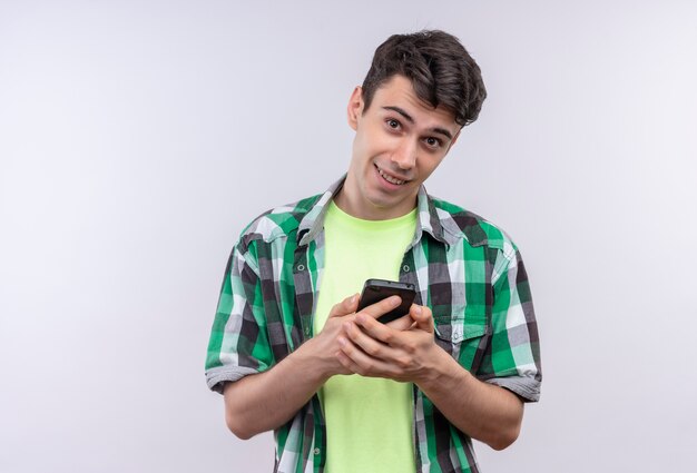 Foto gratuita sonriente joven caucásico vistiendo camisa verde sosteniendo el teléfono con ambas manos sobre fondo blanco aislado