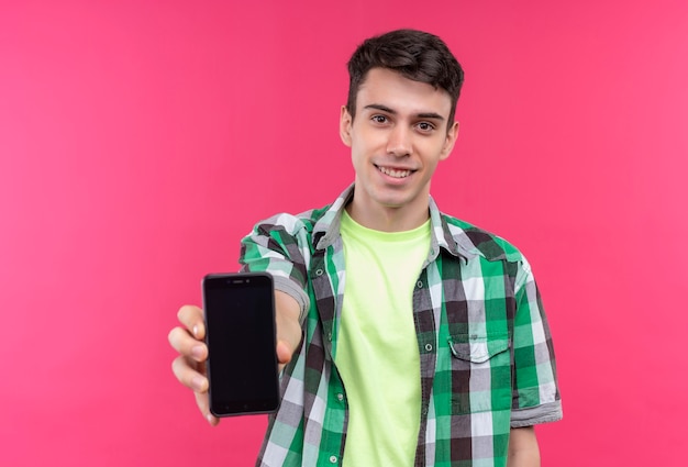 Foto gratuita sonriente joven caucásico vistiendo camisa verde sosteniendo el teléfono a la cámara sobre fondo rosa aislado