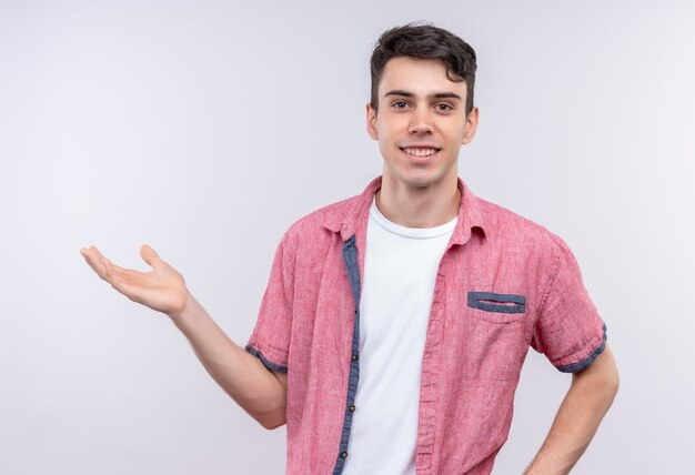 Sonriente joven caucásico vistiendo camiseta rosa levantando la mano sobre fondo blanco aislado