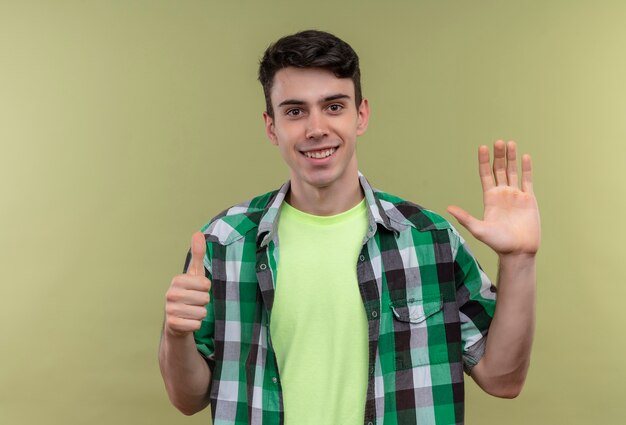 Sonriente joven caucásico vistiendo camiseta verde mostrando diferentes gestos sobre fondo verde aislado