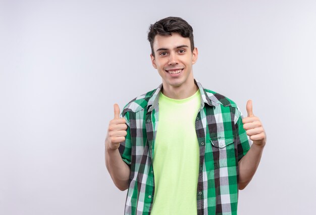 Sonriente joven caucásico vistiendo la camiseta verde sus pulgares hacia arriba sobre fondo blanco aislado