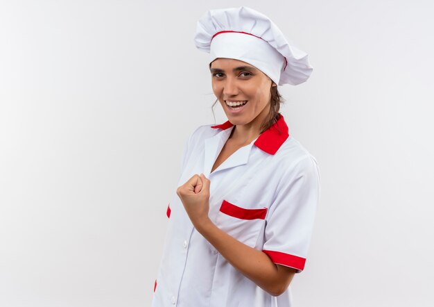 Sonriente joven cocinera vistiendo uniforme de chef haciendo gesto fuerte con espacio de copia