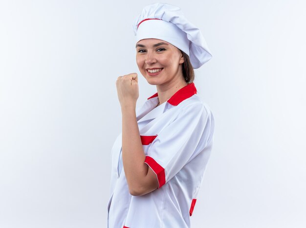 Sonriente joven cocinera vistiendo uniforme de chef mostrando sí gesto aislado sobre fondo blanco.