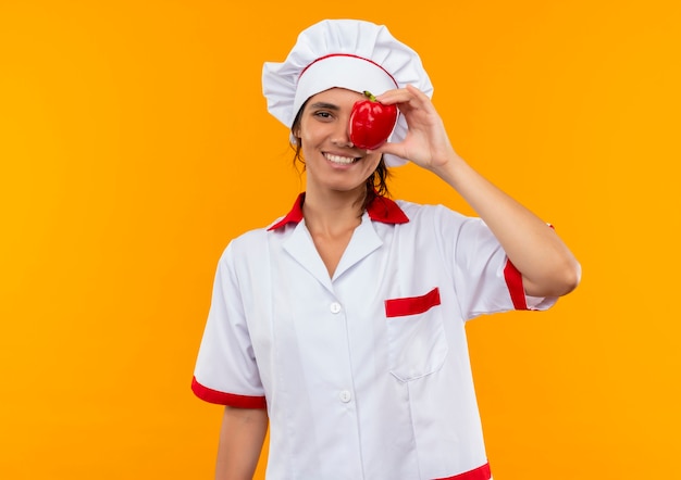 Sonriente joven cocinera vistiendo uniforme de chef ojo cubierto con pimienta con espacio de copia