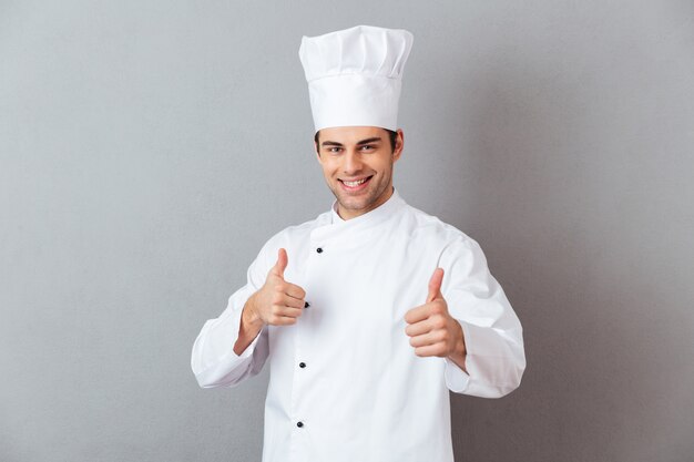 Sonriente joven cocinero emocional con los pulgares para arriba.