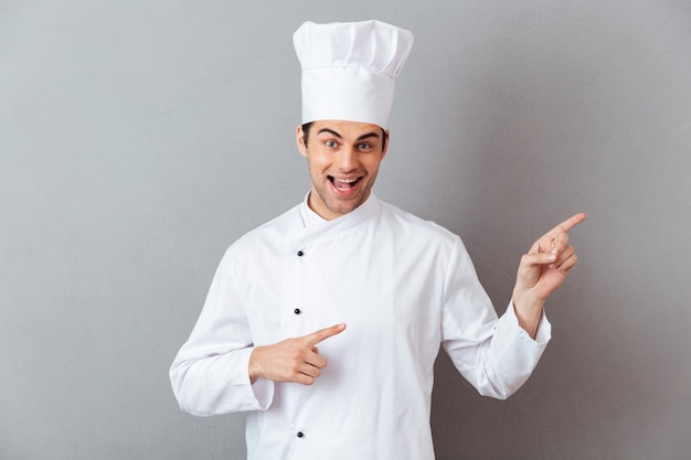 Foto gratuita sonriente joven cocinero en uniforme apuntando.