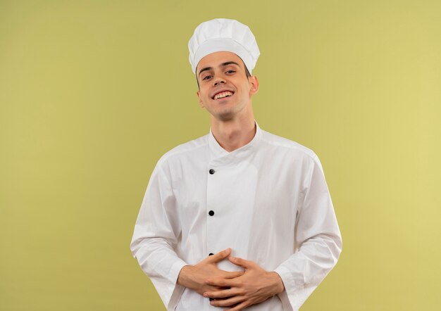 Sonriente joven cocinero vistiendo uniforme de chef poniendo las manos sobre el estómago con espacio de copia