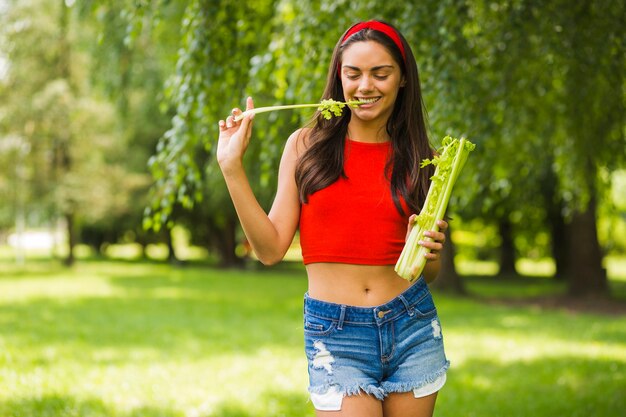 Sonriente joven comiendo apio fresco en el parque