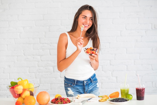 Foto gratuita sonriente joven comiendo ensalada de fruta saludable