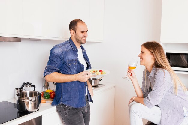 Sonriente joven comiendo ensalada y su esposa bebiendo alcohol