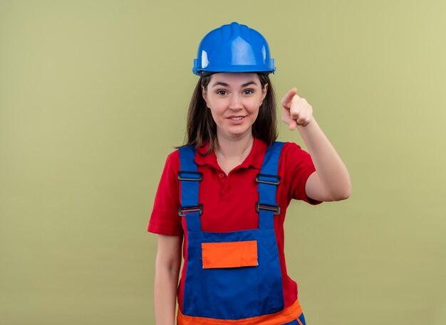 Sonriente joven constructor con casco de seguridad azul apunta hacia adelante y mira a cameraon aislado fondo verde con espacio de copia