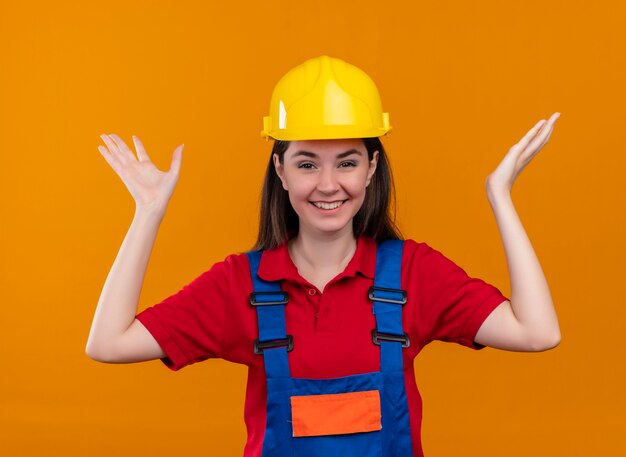 Sonriente joven constructor levanta las manos sobre fondo naranja aislado