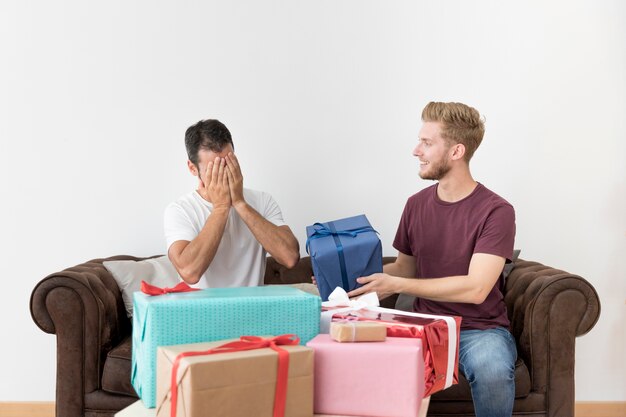 Sonriente joven dando caja de regalo envuelto a su amigo tímido