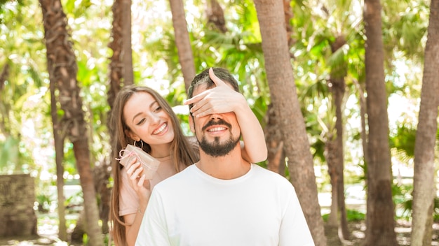 Sonriente joven dando un regalo sorpresa a su novio en el bosque