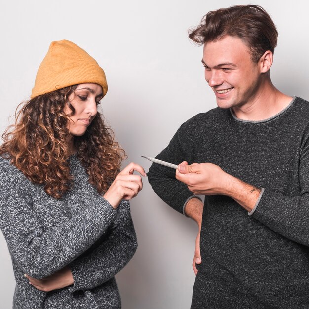 Sonriente joven dando termómetro a su novia