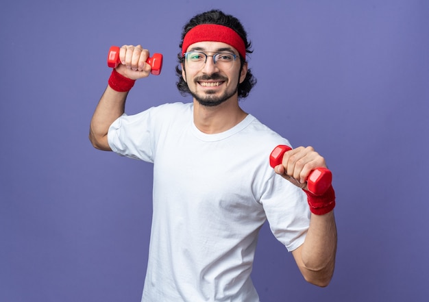 Sonriente joven deportivo vistiendo diadema con muñequera ejercicio con pesas