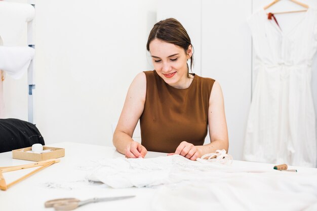 Sonriente joven diseñador de moda trabajando en vestido en estudio