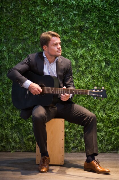 Sonriente joven disfrutando de tocar la guitarra en el café