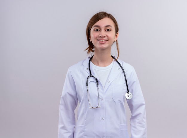 Sonriente joven doctora vistiendo bata médica y estetoscopio en pared blanca aislada con espacio de copia