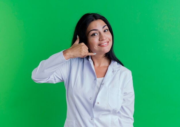 Sonriente joven doctora vistiendo bata médica mirando haciendo gesto de llamada