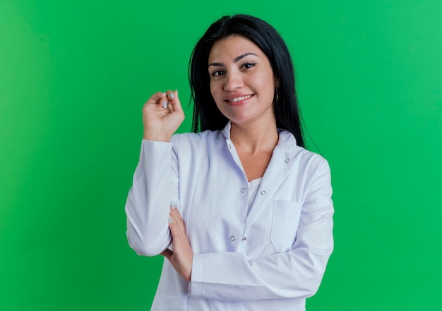 Sonriente joven doctora vistiendo bata médica mirando poniendo la mano en el brazo manteniendo otro en el aire