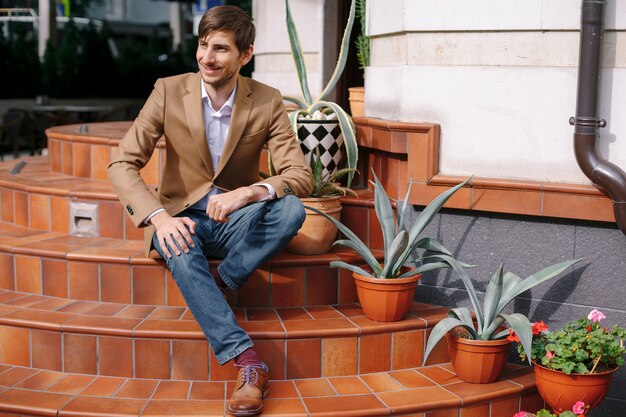 Sonriente joven elegante sentado al aire libre en escaleras circulares vintage