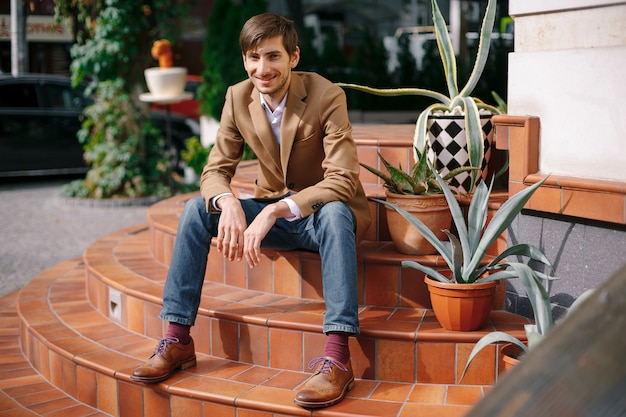 Sonriente joven elegante sentado al aire libre en escaleras circulares vintage